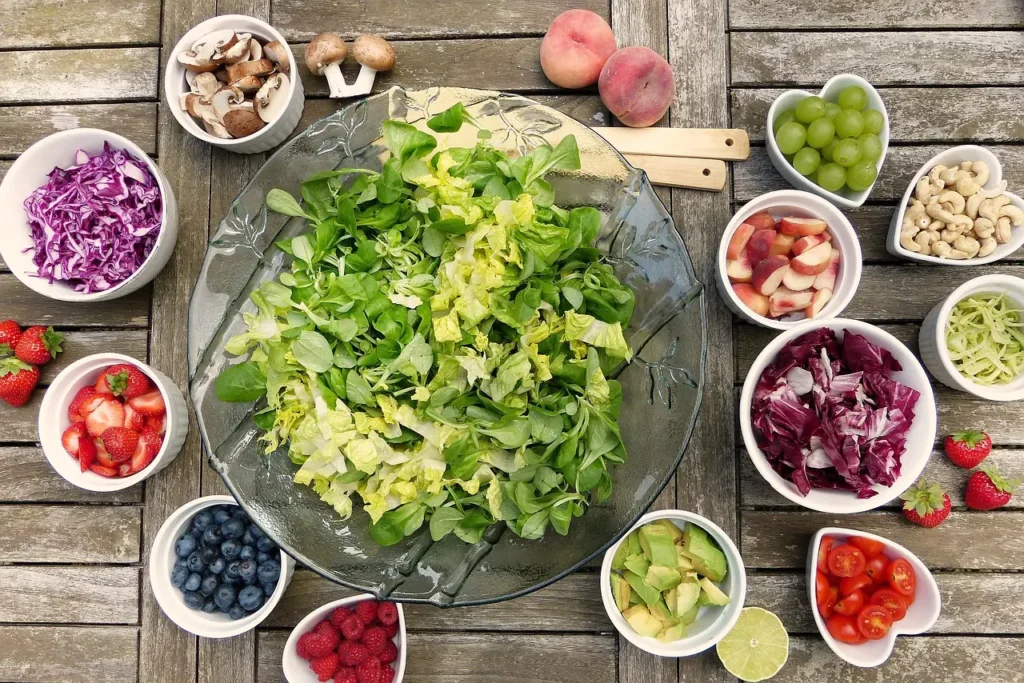 A big bowl of colorful salad with small bowls of salad, fruit and nuts around it.