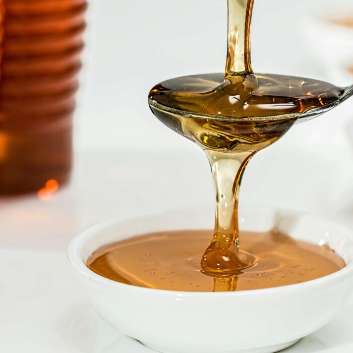 Honey dripping on to a spoon, spilling over in to a white bowl