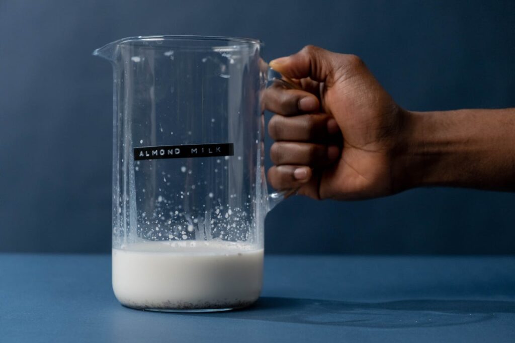 A hand holding a glass jug with a sticker labeled Almond milk