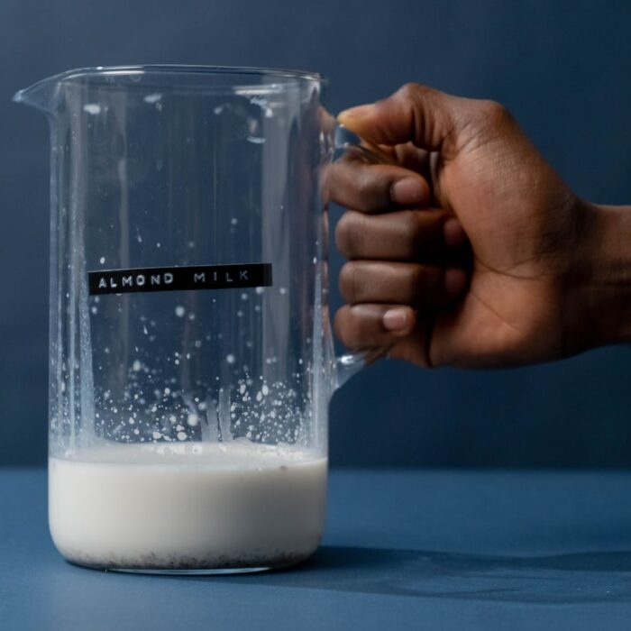 A hand holding a glass jug with a sticker labeled Almond milk