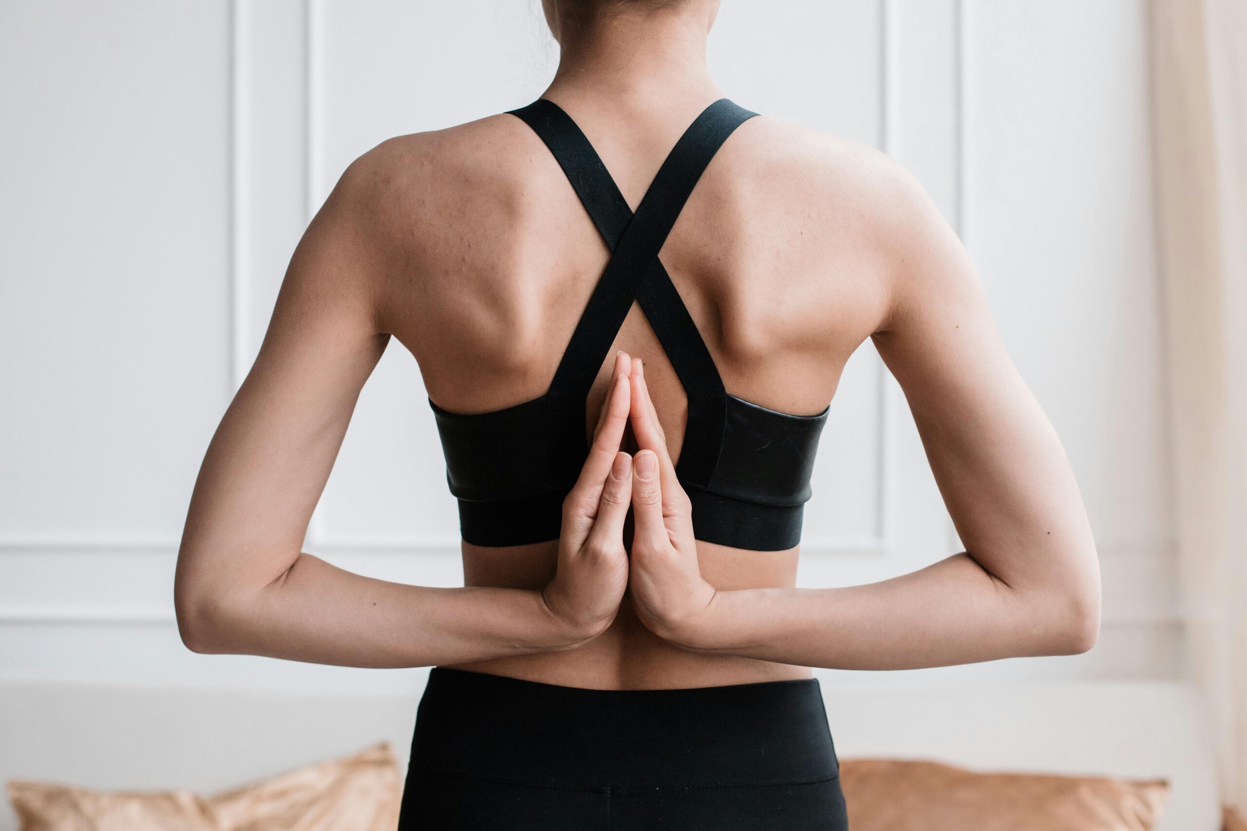 A woman in gym gear with her hands behind her back, pressing her palms together