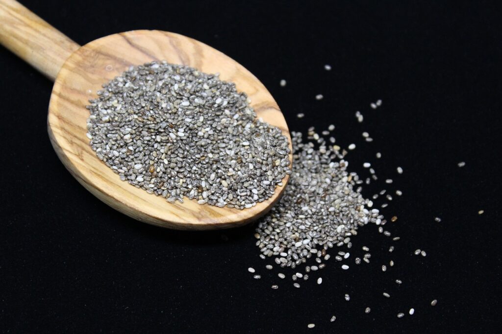 Chia seeds spilling from a Wooden spoon onto a black worktop