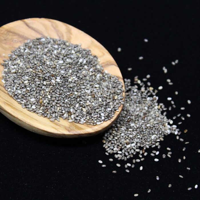 Chia seeds spilling from a Wooden spoon onto a black worktop