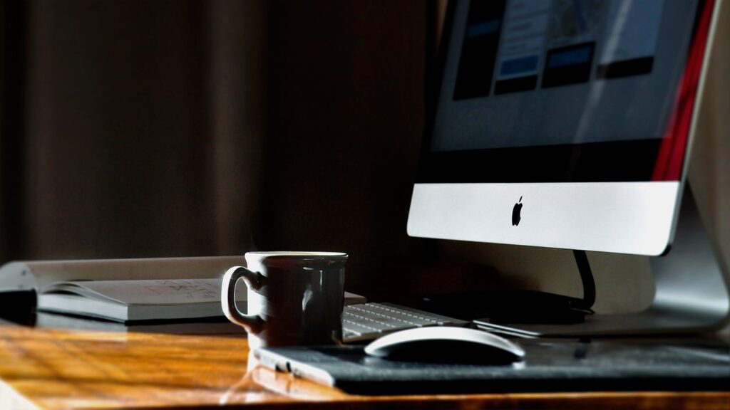 A work desk with an iMac, mouse, and coffee cup on top.