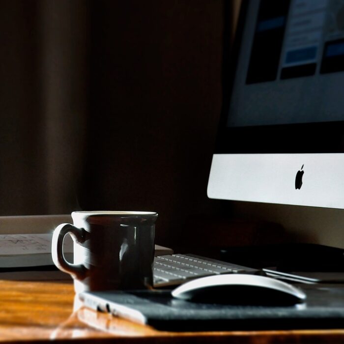 A work desk with an iMac, mouse, and coffee cup on top.