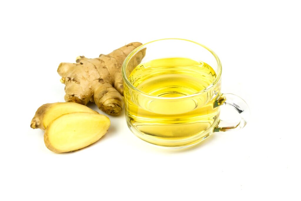 A ginger piece snapped in two next to a hot cup of ginger tea in a glass tumbler