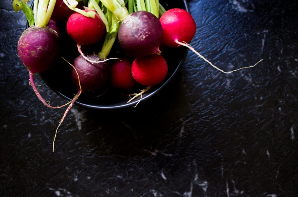 A bird's-eye view of a bunch of radishes in a bowl placed on a table.