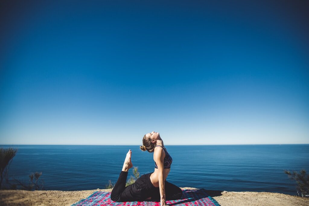 A woman stretching on a mat with the ocean in the background.