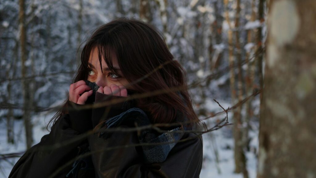 A woman outside in the cold, lifting her jacket to cover her nose, keeping warm in the chilly weather.