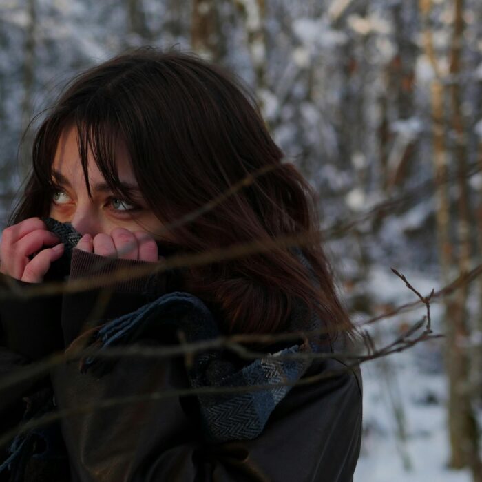 A woman outside in the cold, lifting her jacket to cover her nose, keeping warm in the chilly weather.