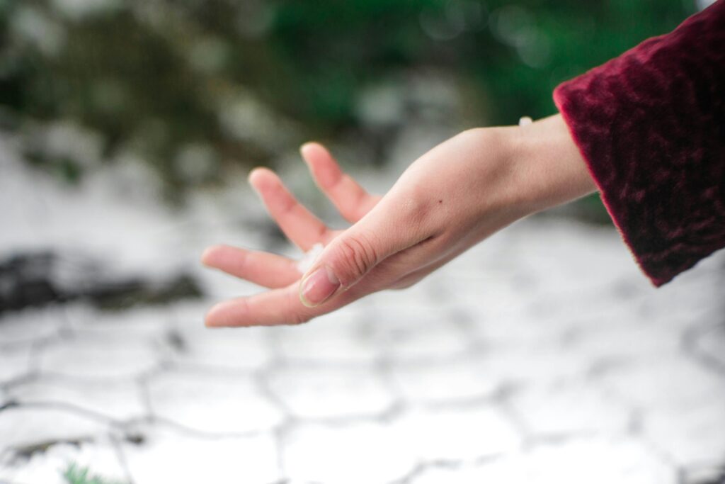 A woman holding her hand out in the cold, frosty outdoors.