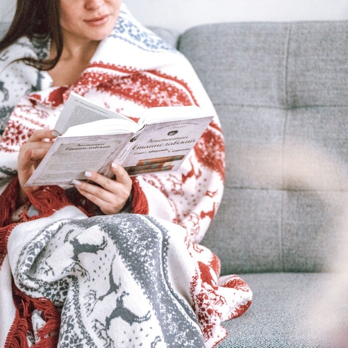 A woman wrapped in a blanket, sitting on a cozy settee, reading a book