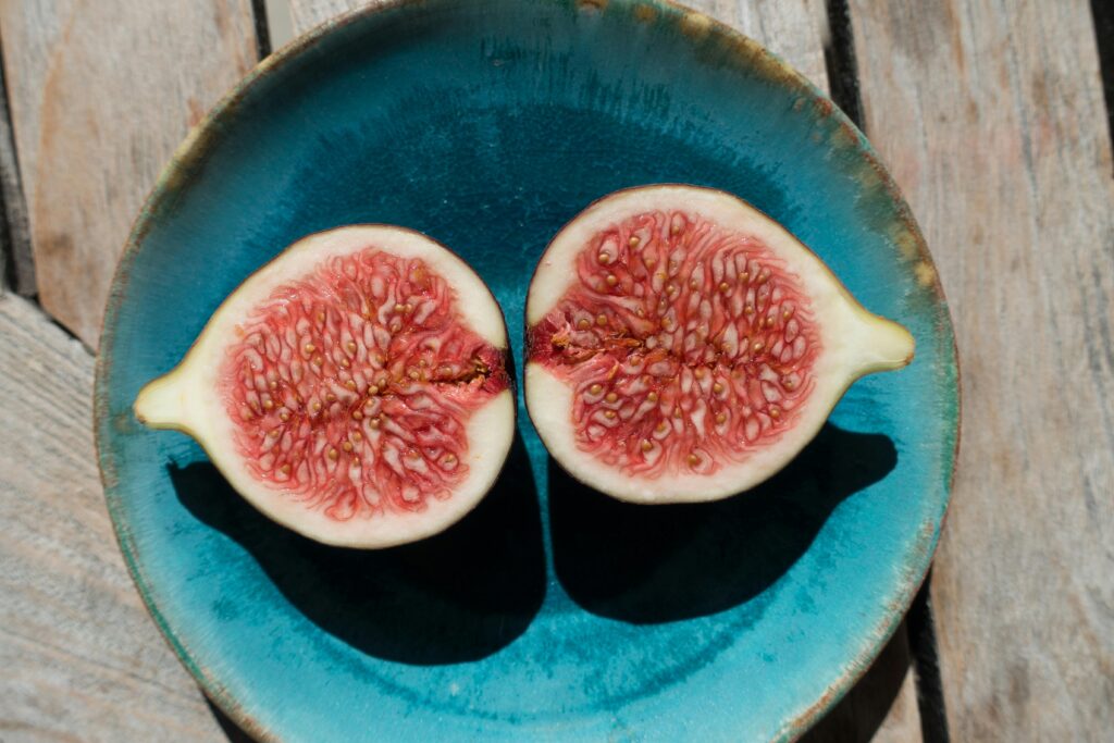 A split-open fig displayed on a plate, placed on a wooden table, showcasing its rich, vibrant interior.