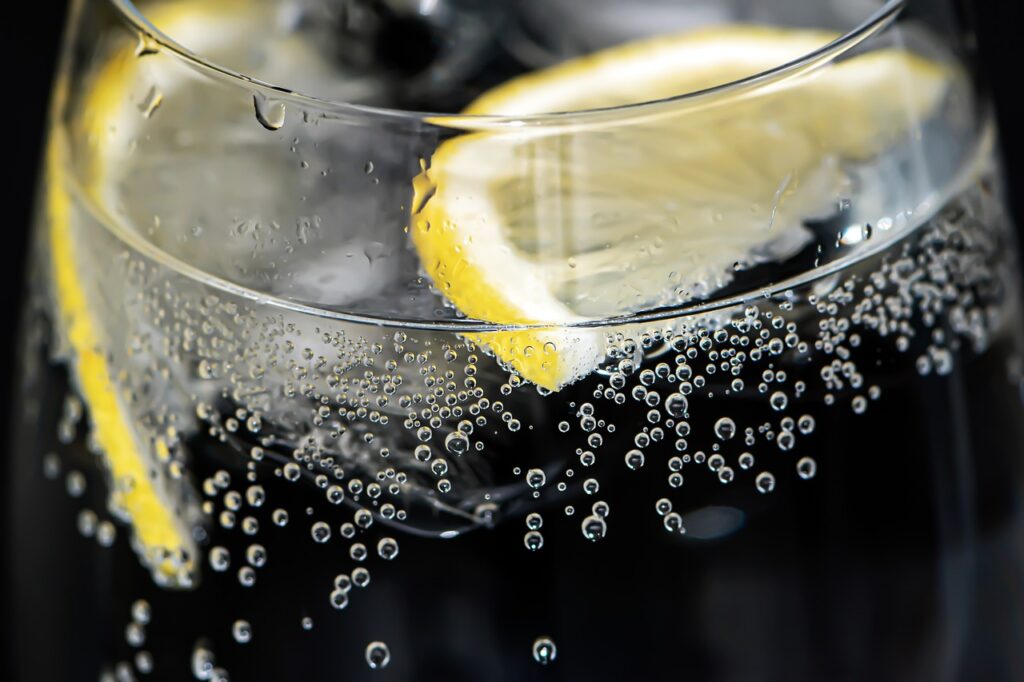 Two fresh lemon slices floating in a crystal-clear glass of water, catching the light with a vibrant, refreshing glow