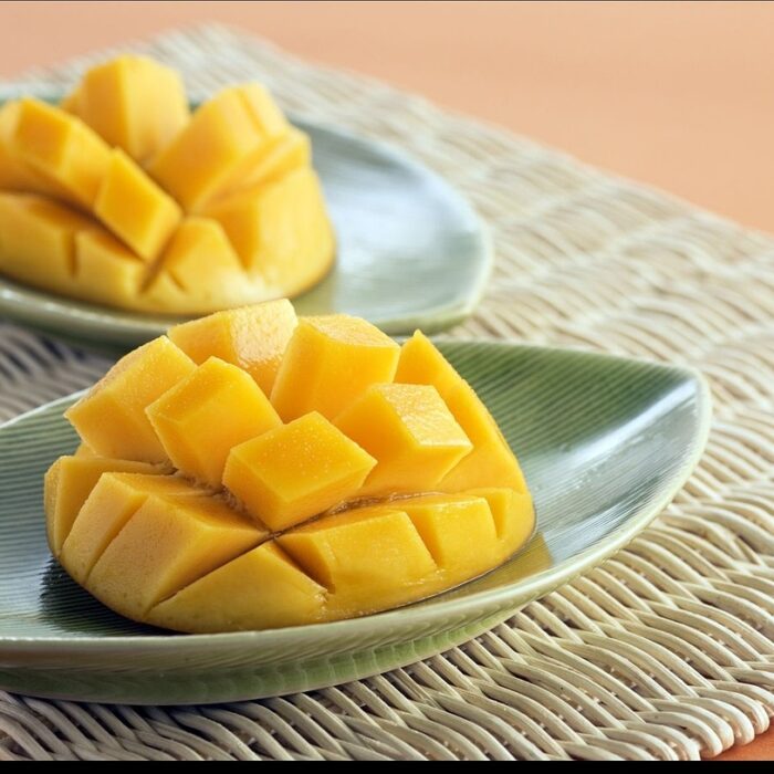 A mango cut in half on each plate, with the flesh cubed but left intact inside the fruit.