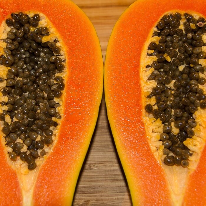 A papaya sliced in half, placed on a wooden table