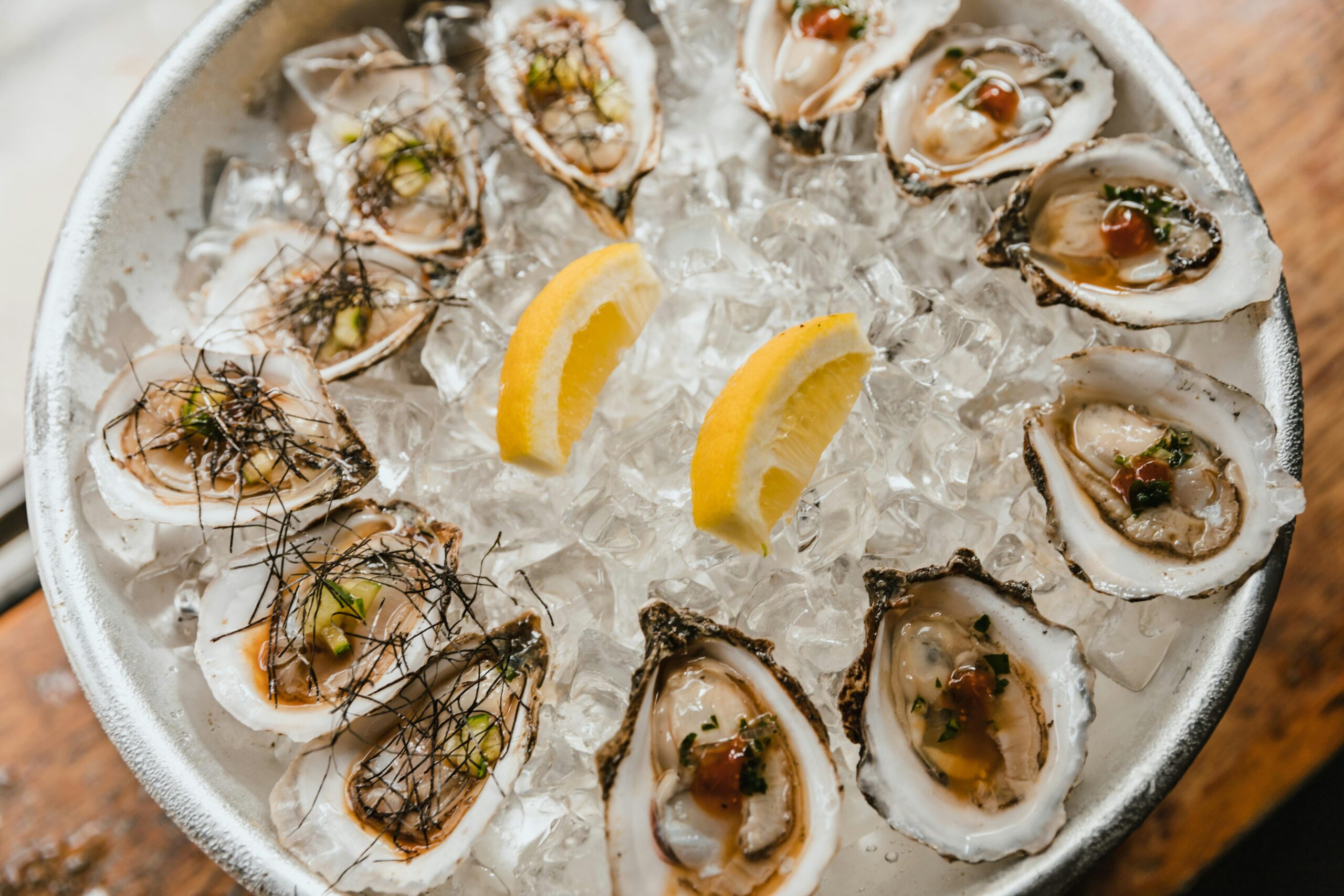 A bowl of ice with oysters arranged in a circle, featuring two lemon slices placed in the center.