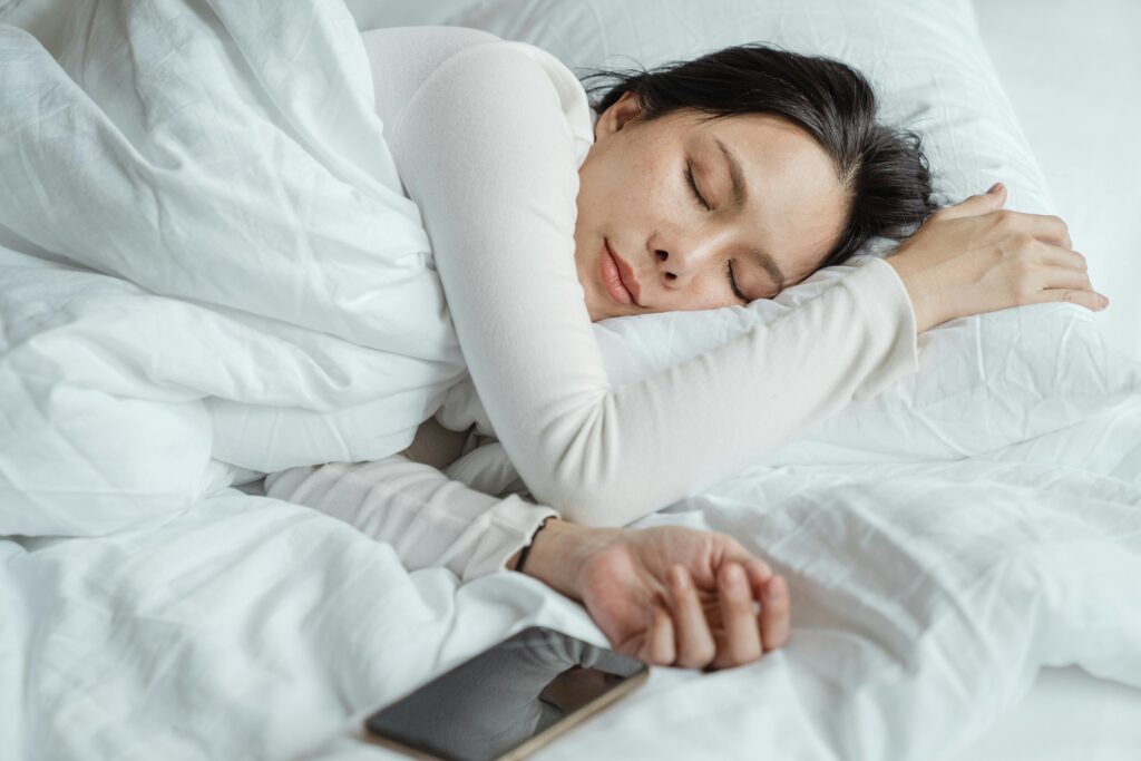 A sleeping woman in bed with her phone beside her.