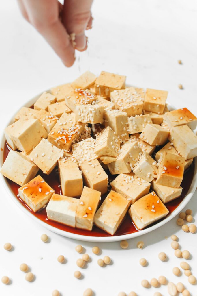 Someone sprinkling sesame seeds on top of a bowl of Tofu