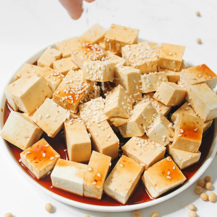 Someone sprinkling sesame seeds on top of a bowl of Tofu