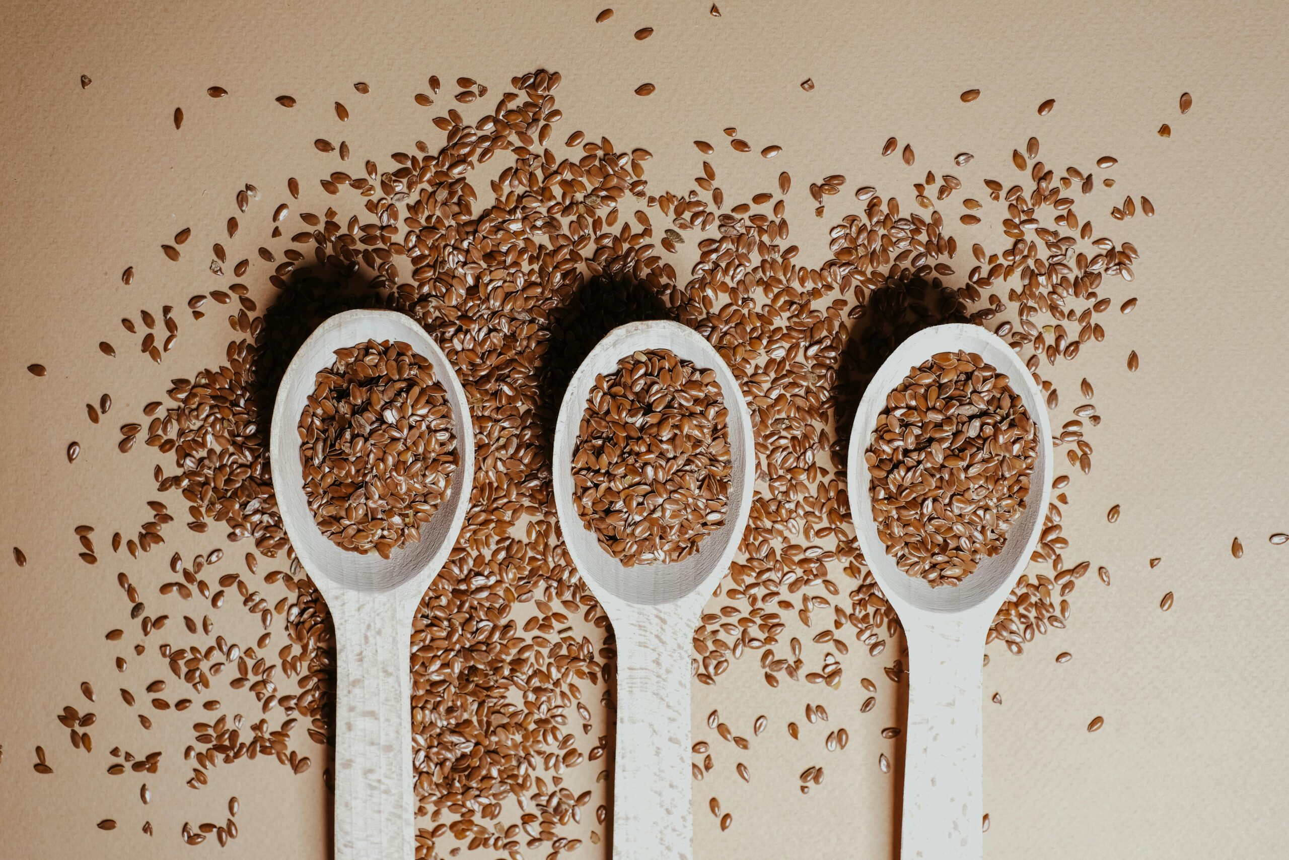 3 spoons covered with Linseed (Flaxseed) spilling on to the surface below